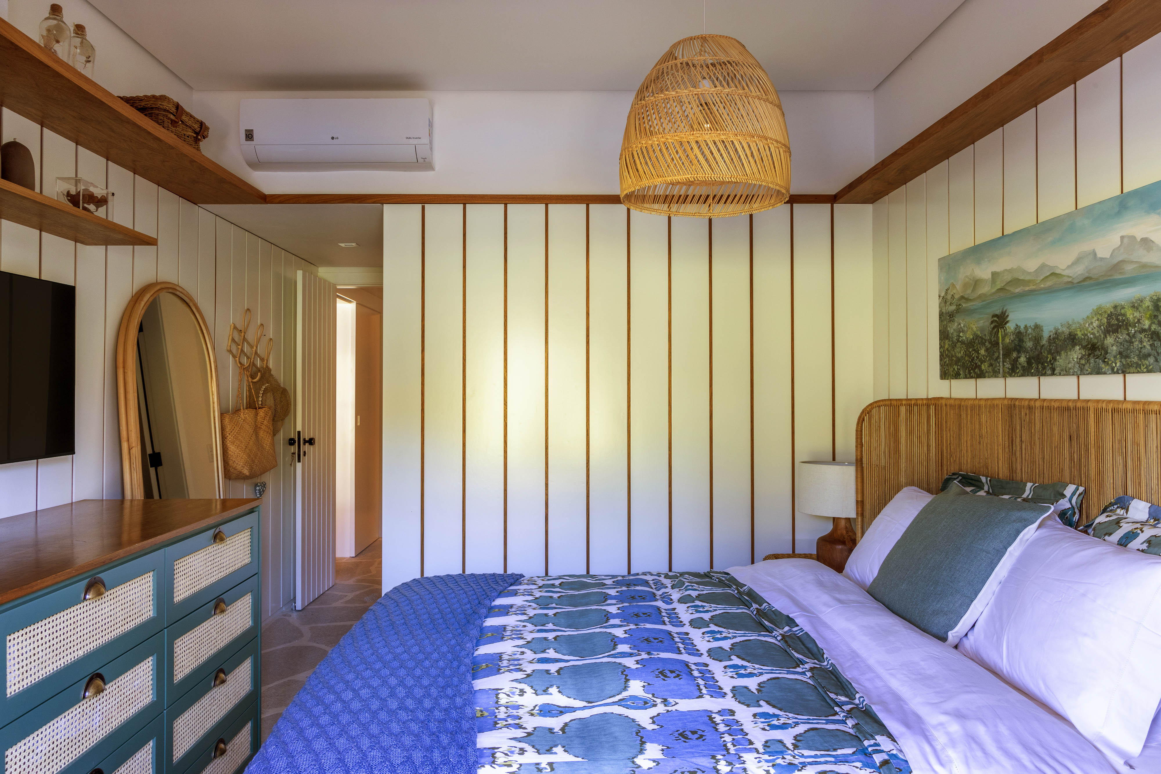 Casa de condomínio de 110 m² tem vista para o canal e décor "praia chic". Projeto de Paola Ribeiro. Na foto, quarto de casal com lambri na parede, móveis de palhinha e TV.