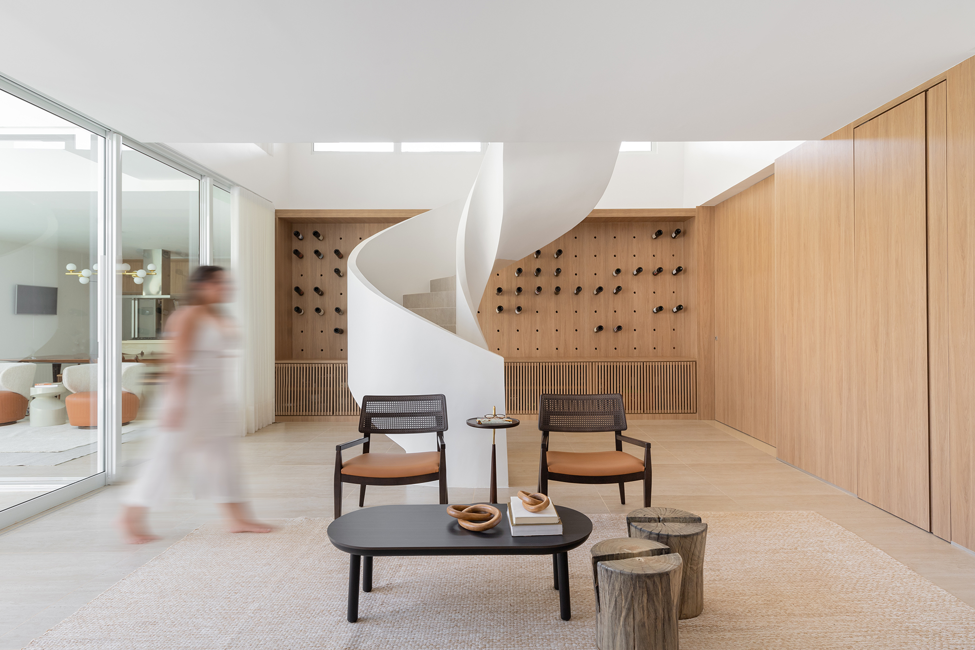 Adega e escada helicoidal se destacam em casa com projeto atemporal. Projeto Traama Arquitetura. Na foto, sala com escada helicoidal e adega na parede.