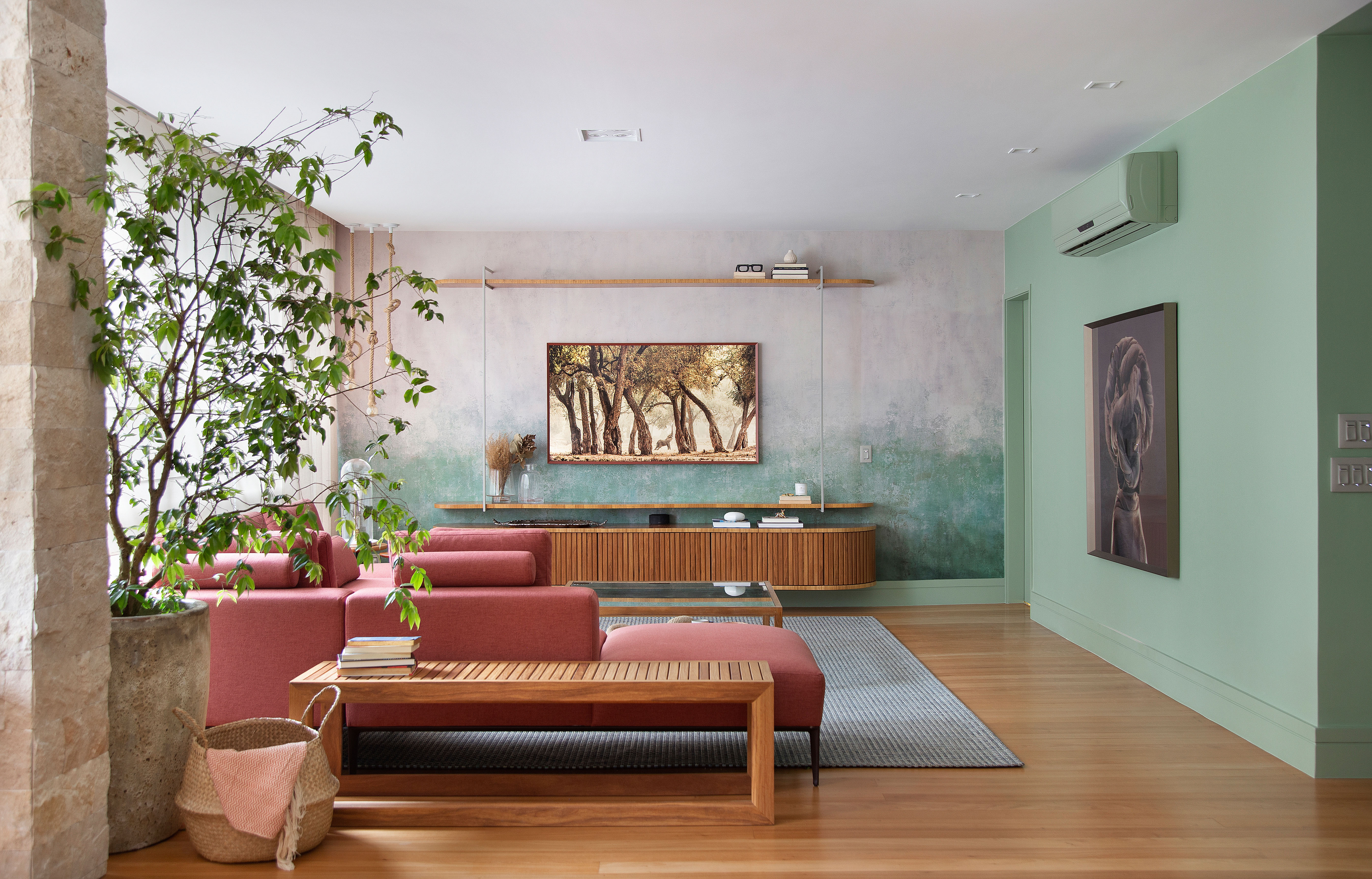 Papel de parede com efeito degradê envelhecido é destaque deste apê. Projeto de Manoela Fleck. Na foto, sala de estar com sofá terracota, banco e vaso.