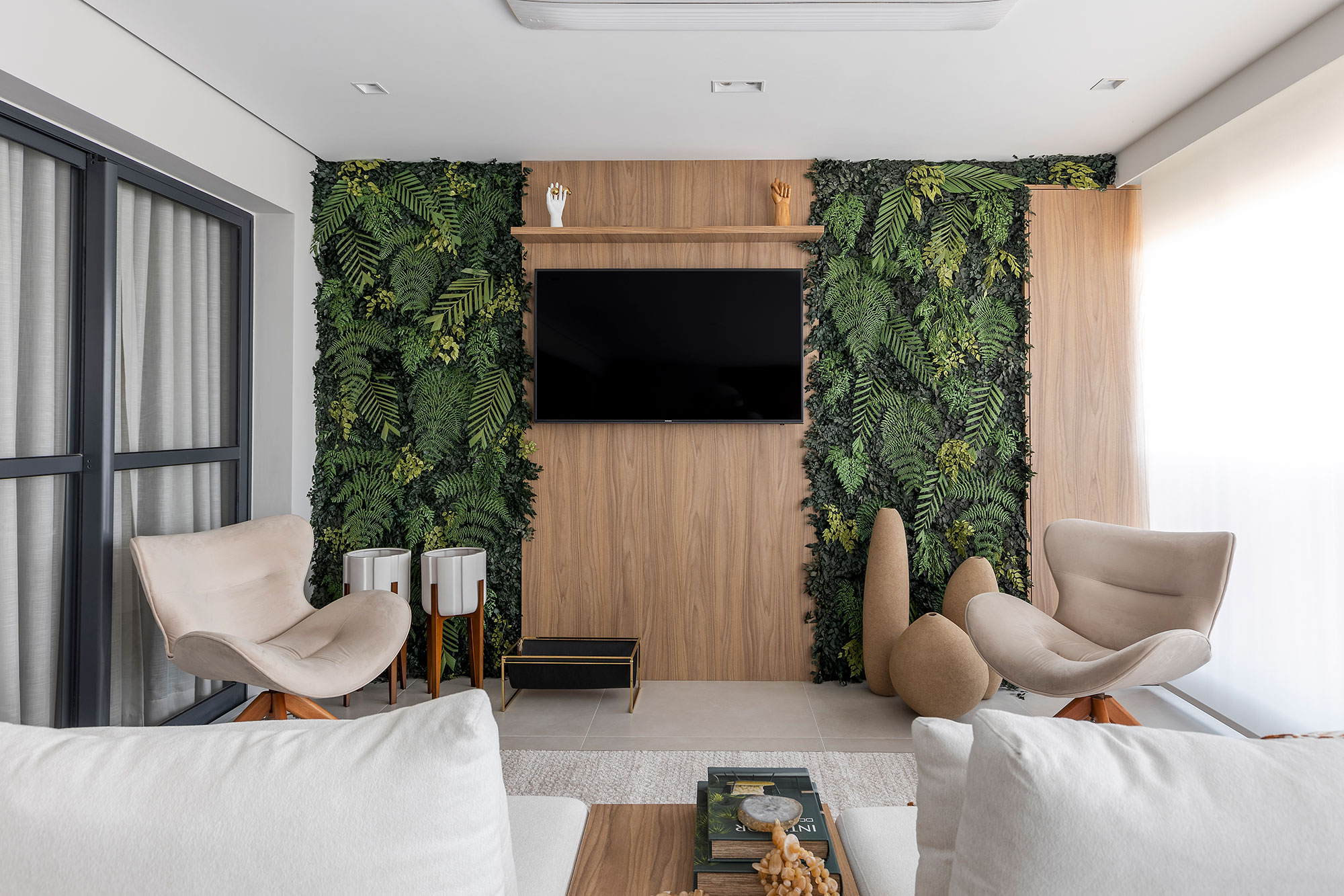 Blaia e Moura Arquitetos privilegia a integração neste apartamento em SP. Na foto, varanda com sofá, TV e jardim vertical.