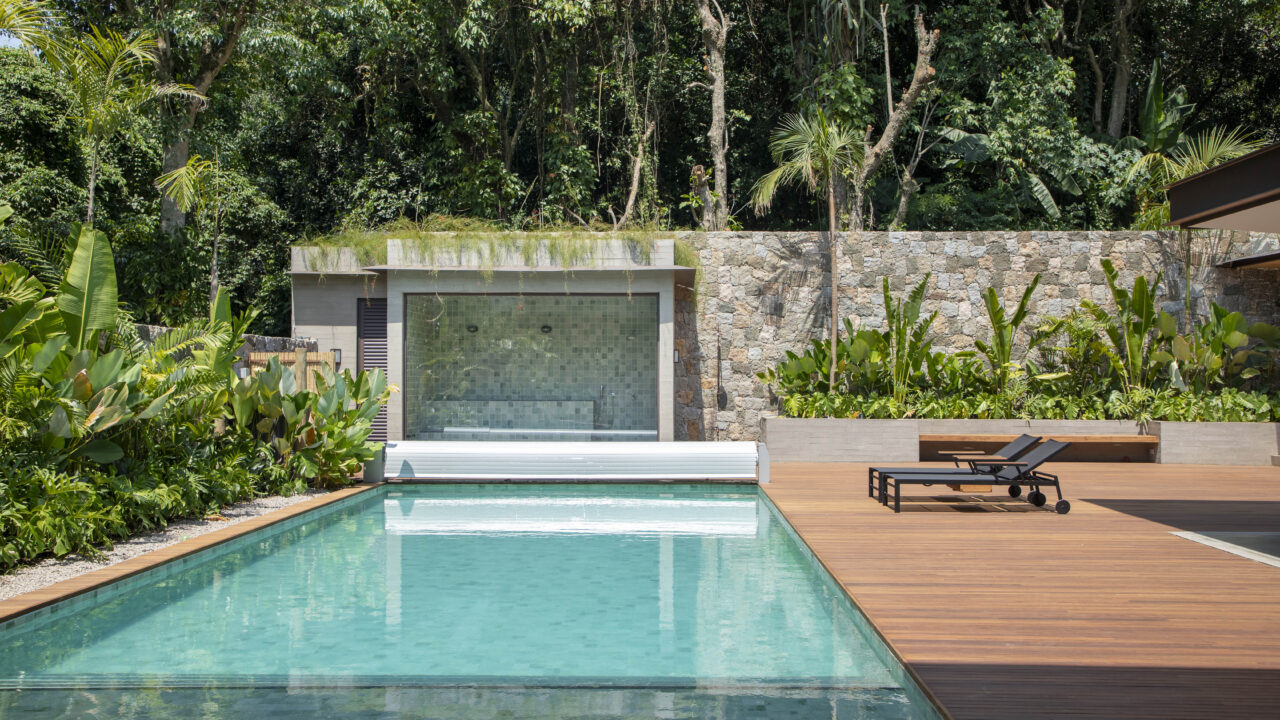 Em aclive, casa de estrutura metálica é erguida acima do nível da rua. Projeto de PKB Arquitetura. Na foto, piscina com deque de madeira e jardim.