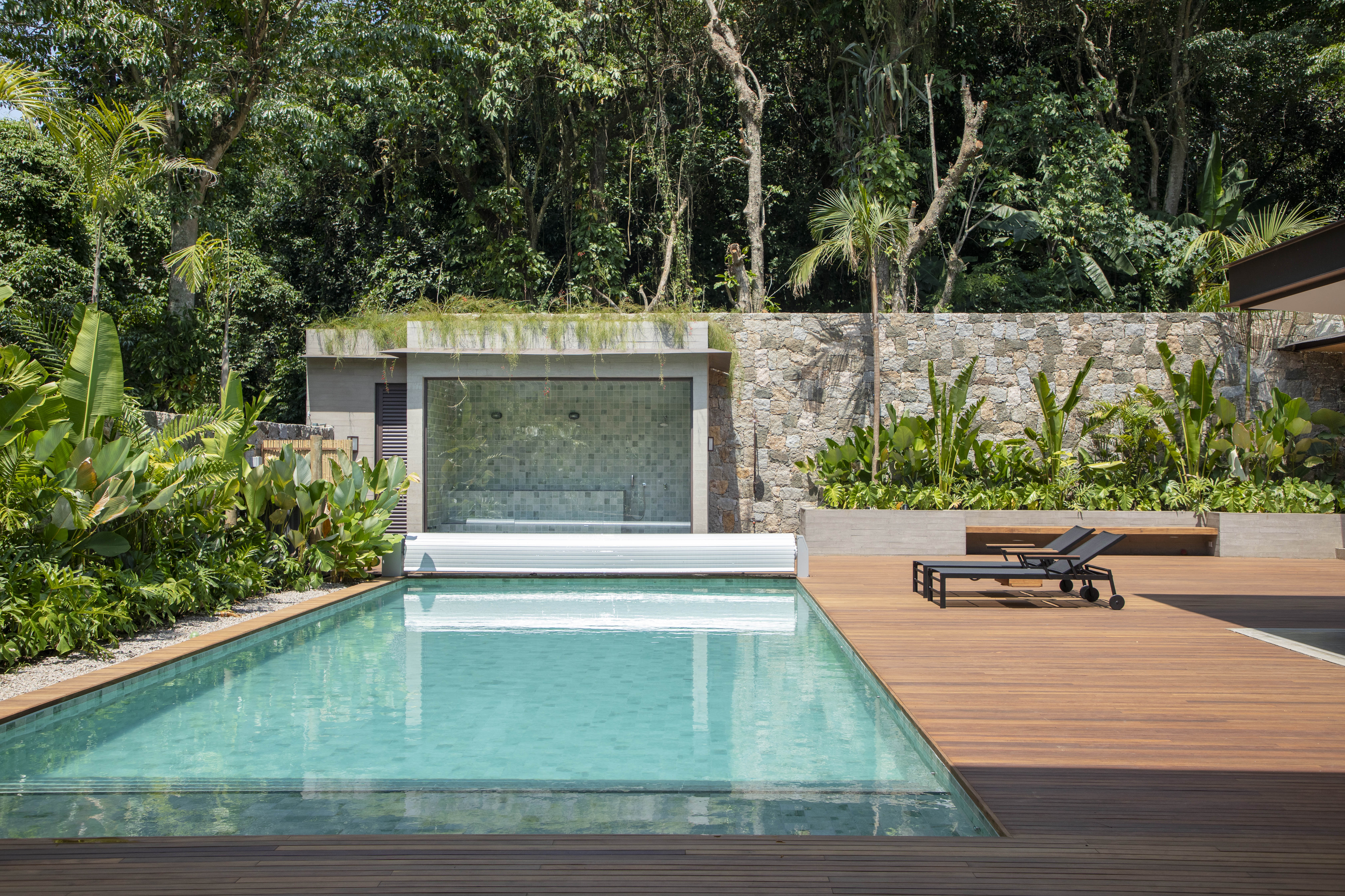 Em aclive, casa de estrutura metálica é erguida acima do nível da rua. Projeto de PKB Arquitetura. Na foto, piscina com deque de madeira e jardim.