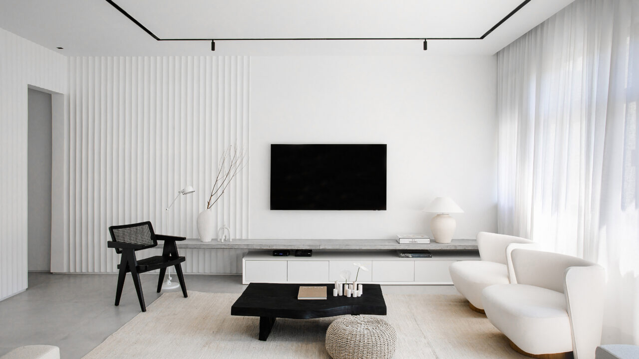 Casal de ingleses troca a casa na Inglaterra por apê minimalista no Rio. Projeto da arquiteta Natalia Lemos. Na foto, sala de estar com tv, parede branca e poltronas.
