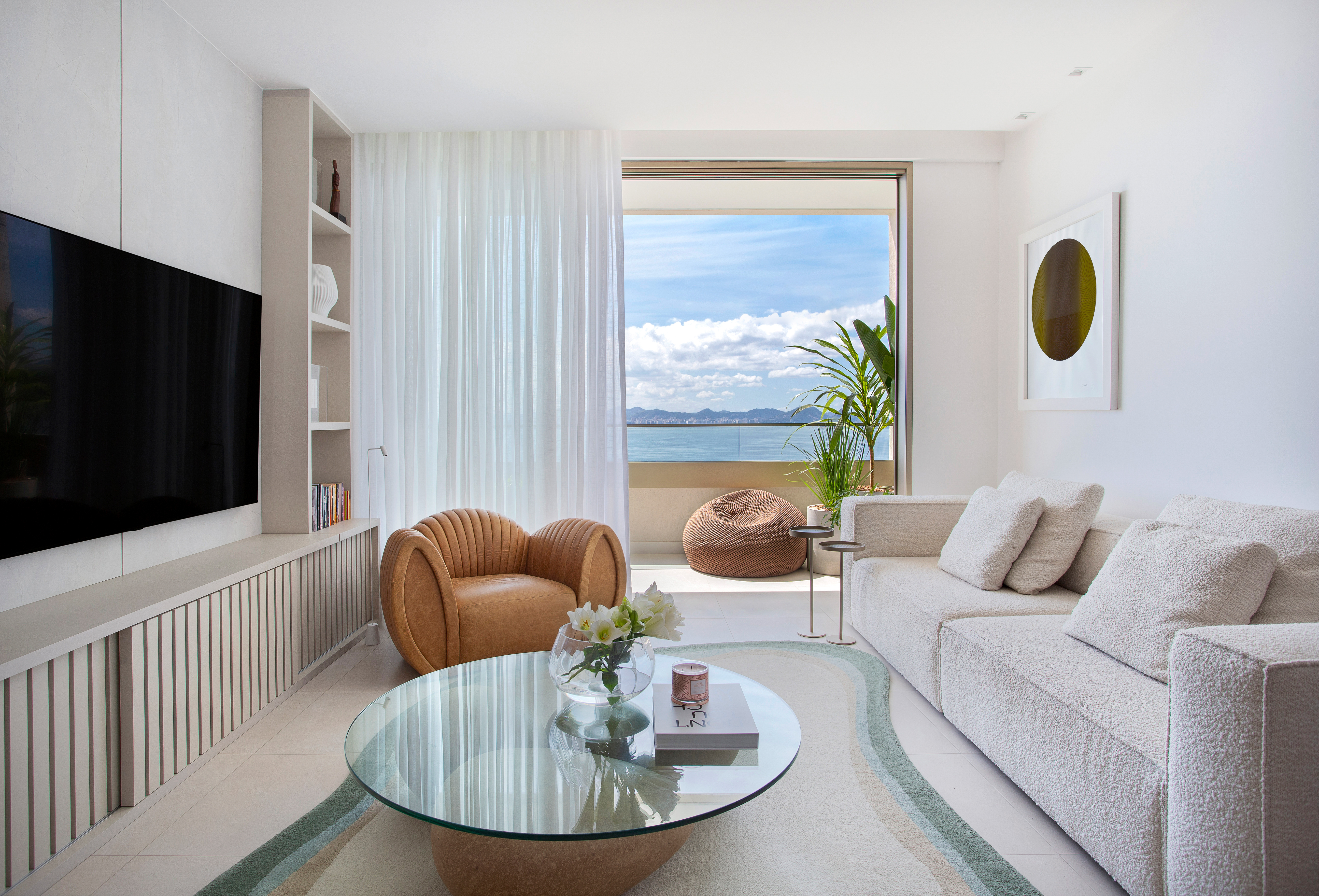 Conheça o lar da atriz Clara Moneke, assinado por Tom Castro. Na foto, sala de estar com vista para o mar, sofá e tapete.