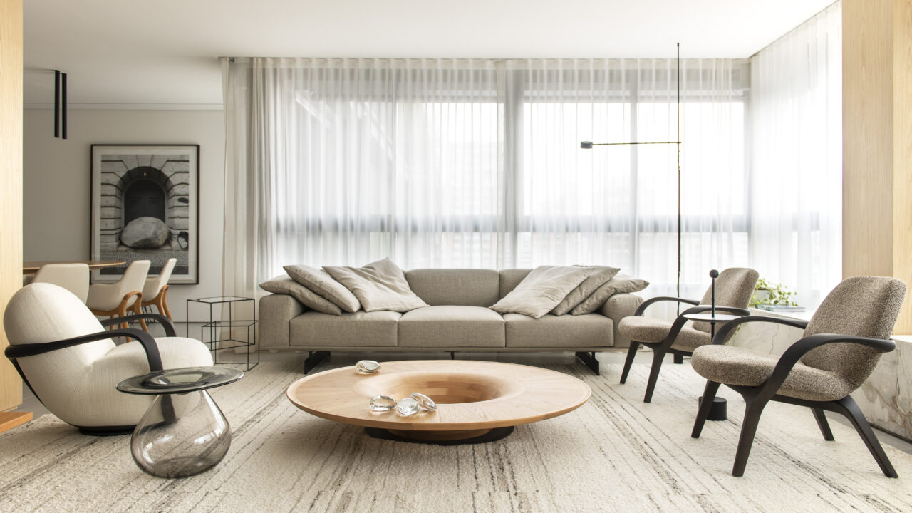 Influências europeias e brasileiras se misturam neste apê em São Paulo. Projeto de Patricia Martinez Arquitetura. Na foto, sala de estar com sofá cinza, poltronas, tapete e cortina.