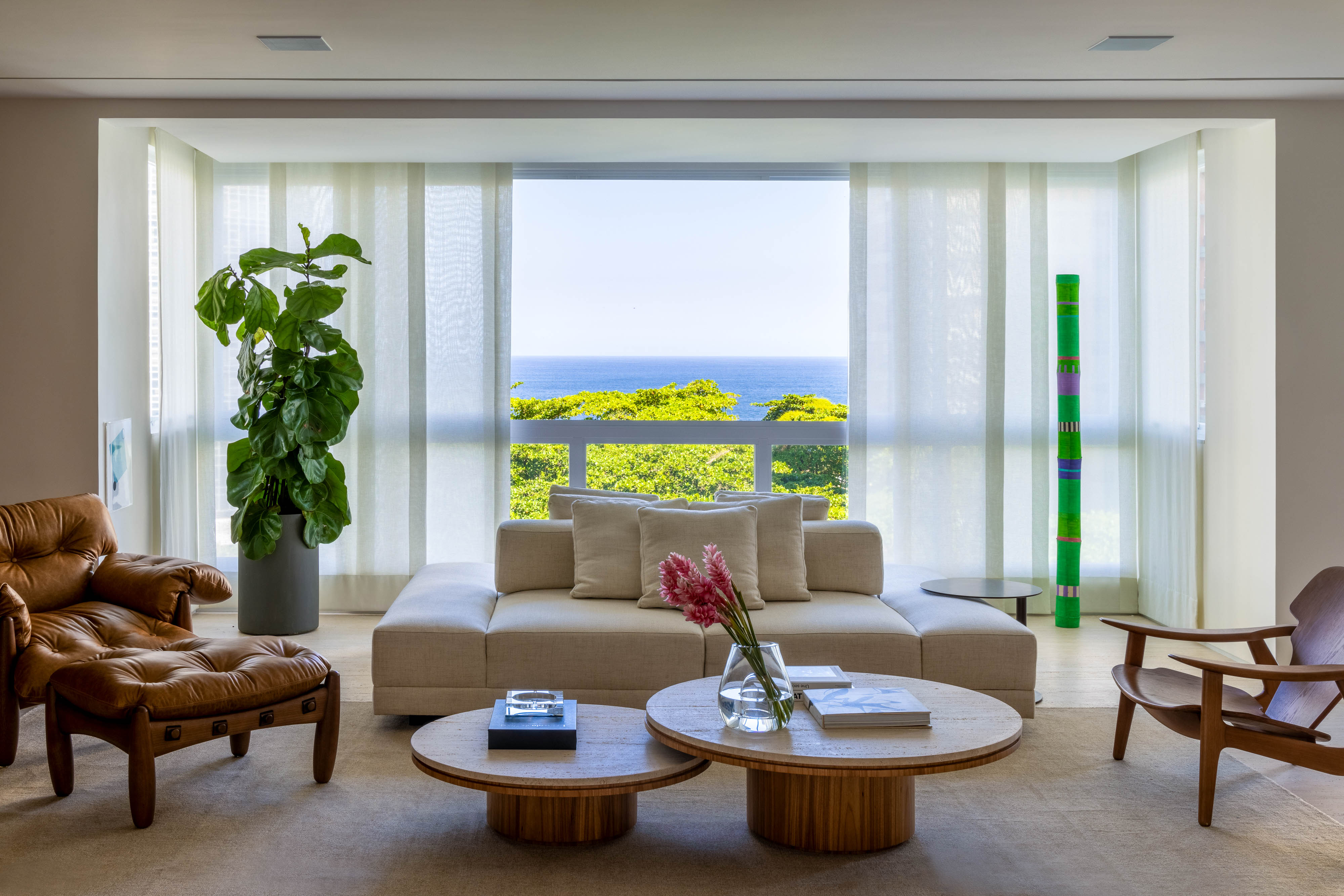 Mar de São Conrado é enquadrado nas janelas deste projeto de LessaZanetta. Na foto, sala de estar com estante de madeira, sofá e poltronas.