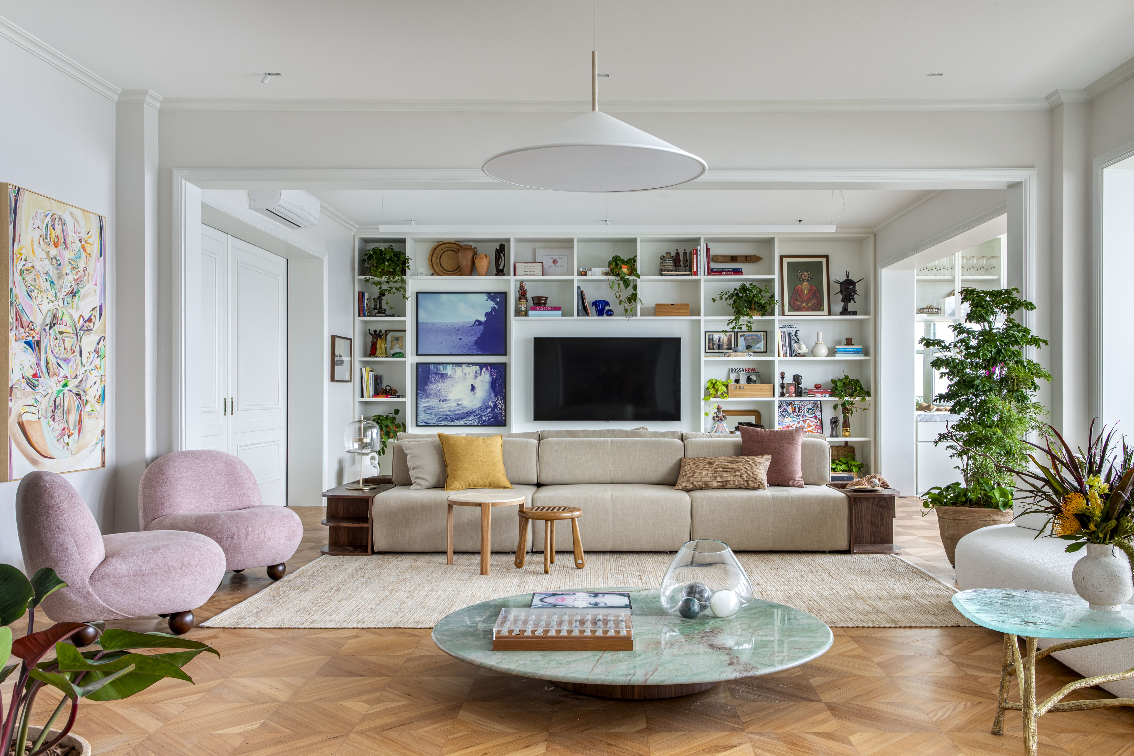 Conheça o apartamento de Taís Araújo e Lázaro Ramos. Projeto de Escala Arquitetura. Na foto, sala com estante, tv e mesa.