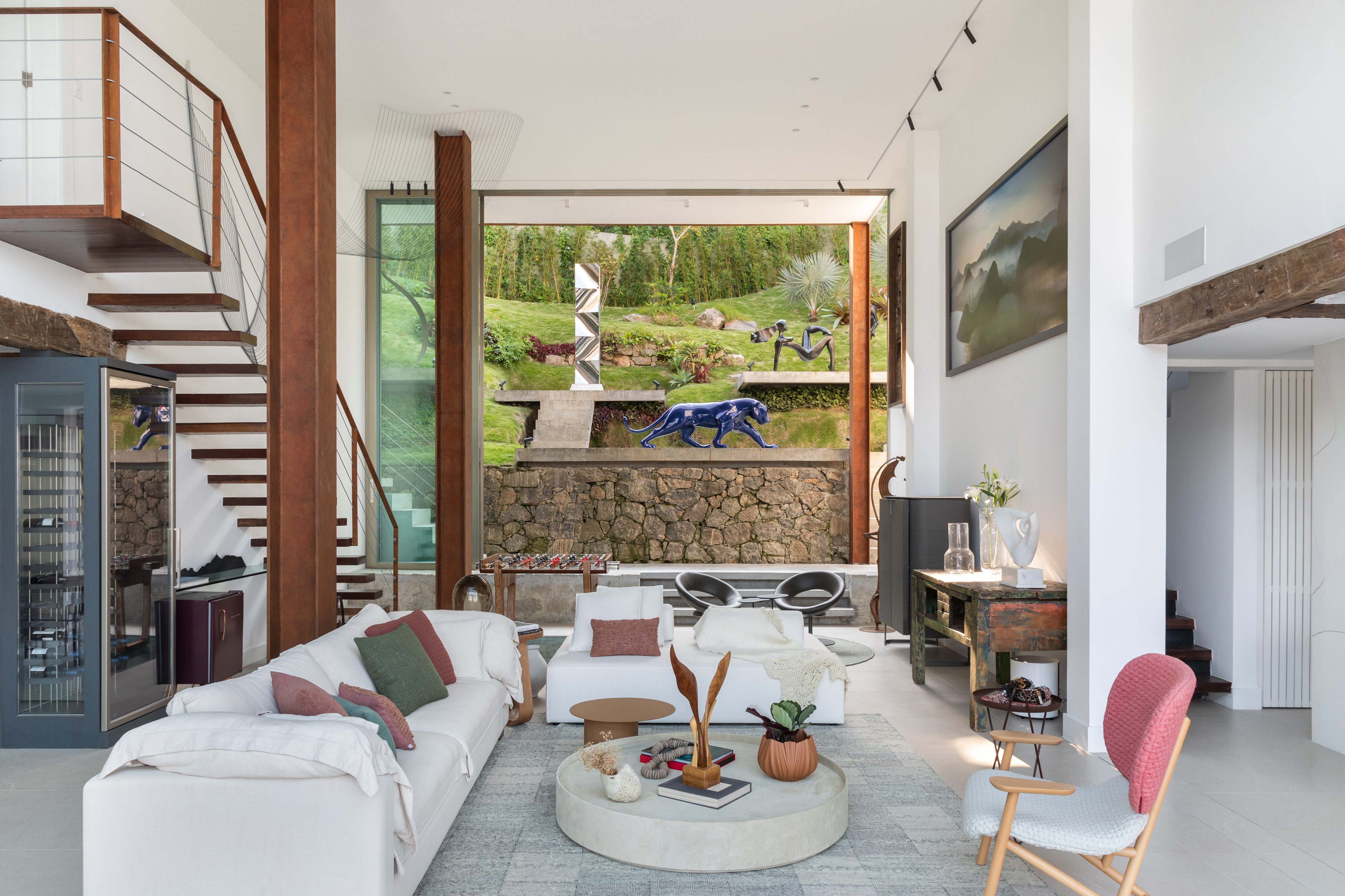 Em frente ao mar, casa une suíte-loft, TV escondida e jardim de esculturas. Projeto de Ketlein Amorim. Na foto, sala de estar com escada e vista para o jardim de esculturas.