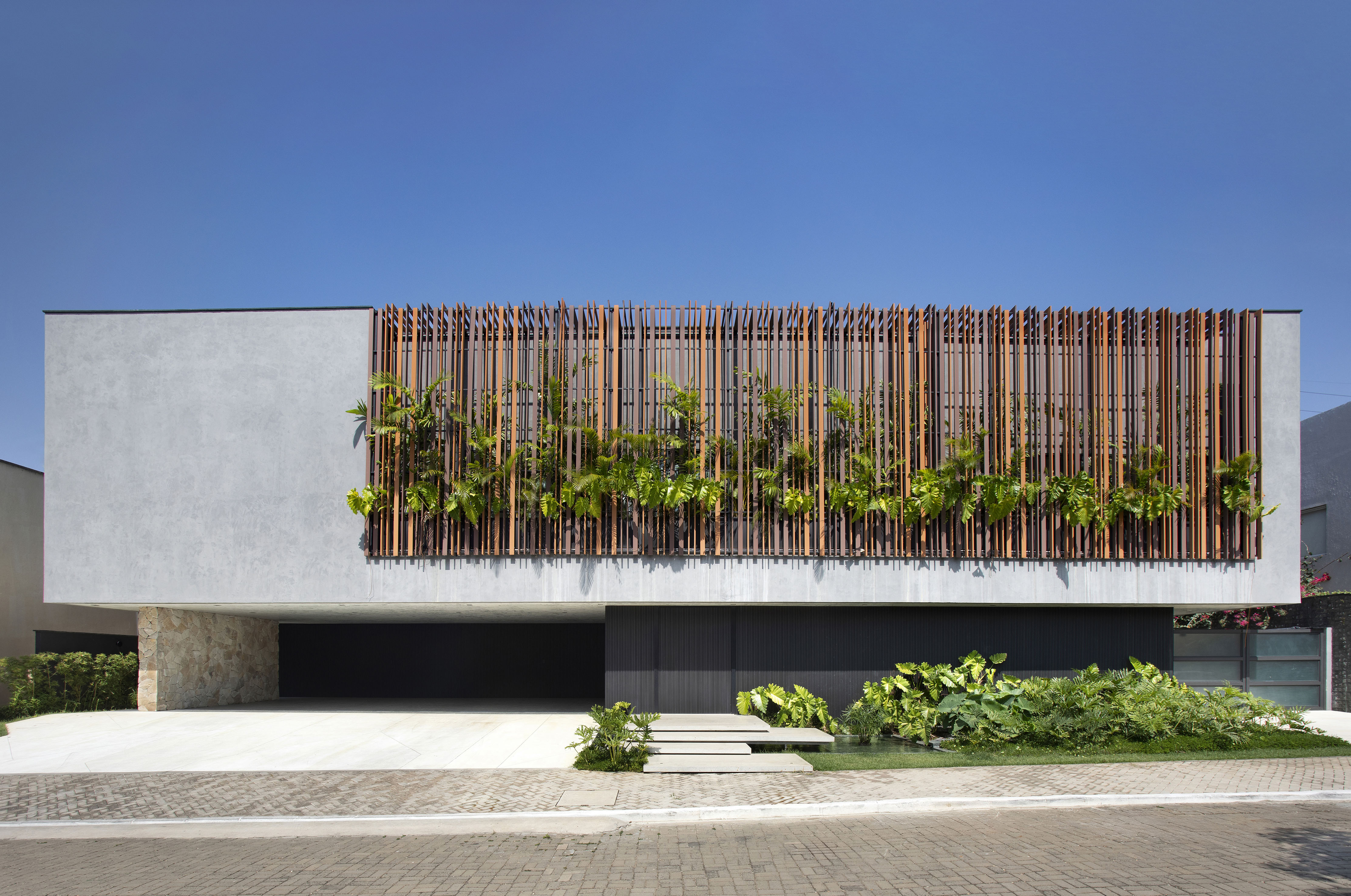 No Piauí, casa com fachada de concreto e brises de madeira parece flutuar. Projeto de Vangii Guerra. Na foto, fachada da casa de concreto e ripas de madeira.